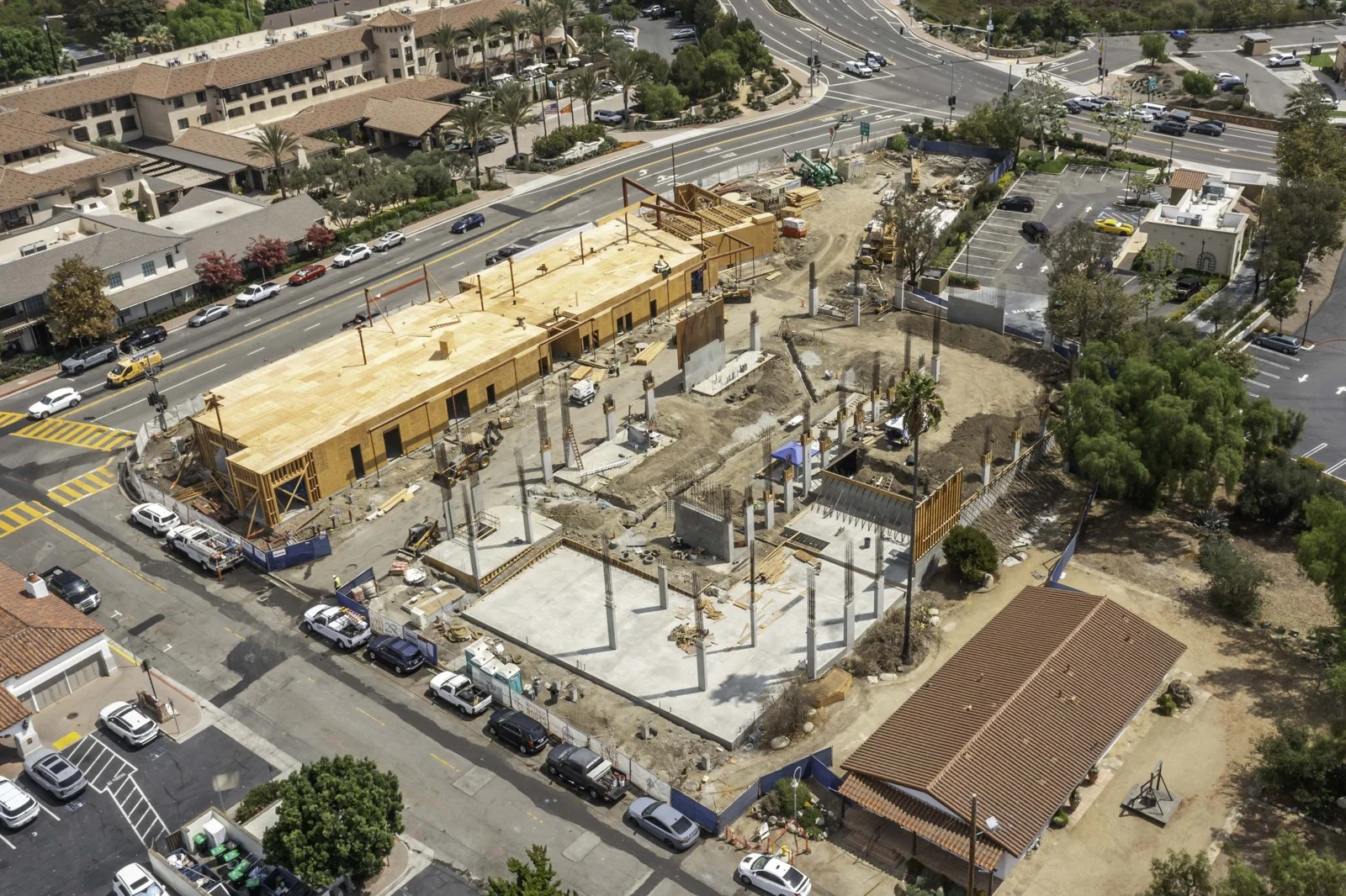 Mission Place construction site with a long wood-sheathed structure, open wall openings, concrete slabs, columns and graded soil.